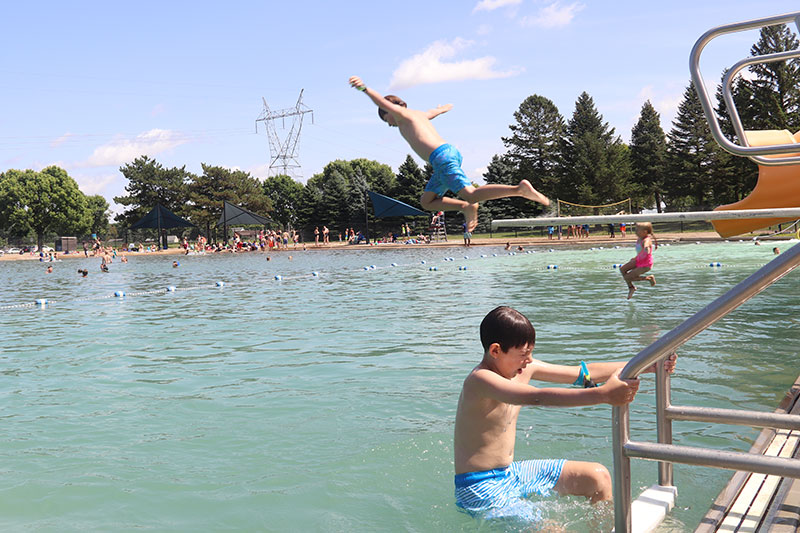 Boy leaps off diving board with boy climbing ladder in foreground