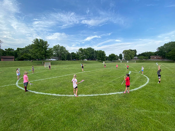 Girls playing lacrosse around a circle outside