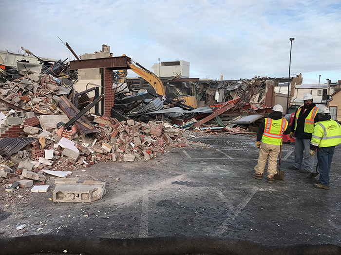 Construction crews watching backhoe take down building